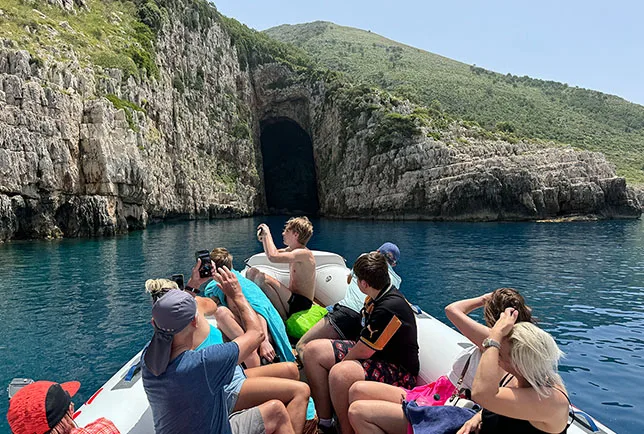 Group of people on a boat, taking photos of the entrance of Haxhi Ali Cave, during a boat trip Vlore, Albania