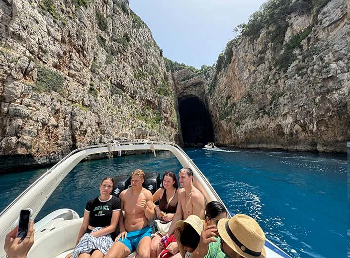 A group of people taking a photo in front of the entrance of Haxhi Ali Cave, during a boat trip in Vlore, Albania