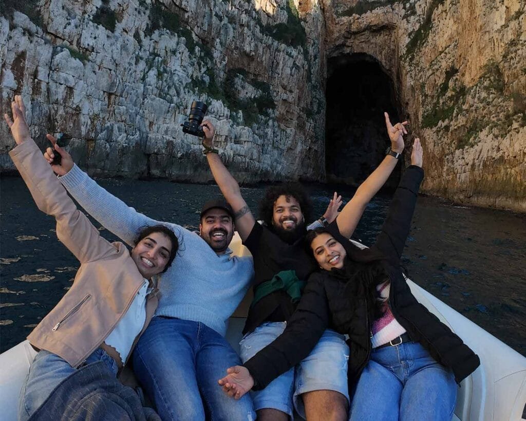 A group of happy people, with the hands in the air, in front of Haxhi Ali Cave, during a boat trip Vlore